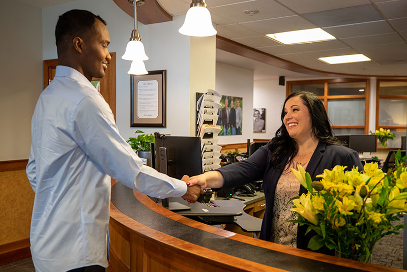 patient and staff member shaking hands at the front desk of the dental office