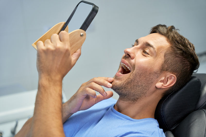 guy looking at teeth through mirror